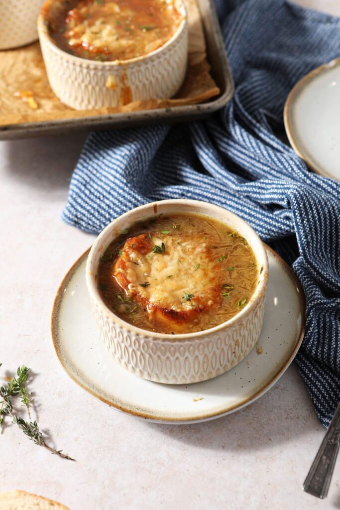 A bowl of French Onion Soup garnished with fresh thyme leaves on a plate with a spoon