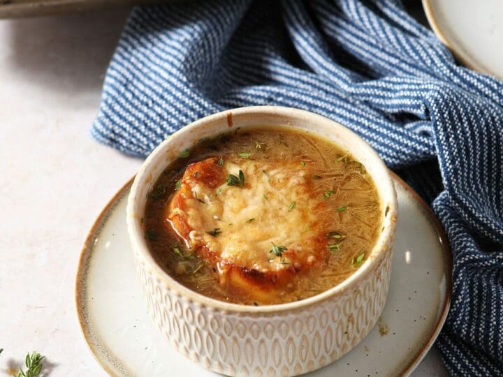 A bowl of French Onion Soup garnished with fresh thyme leaves on a plate with a spoon