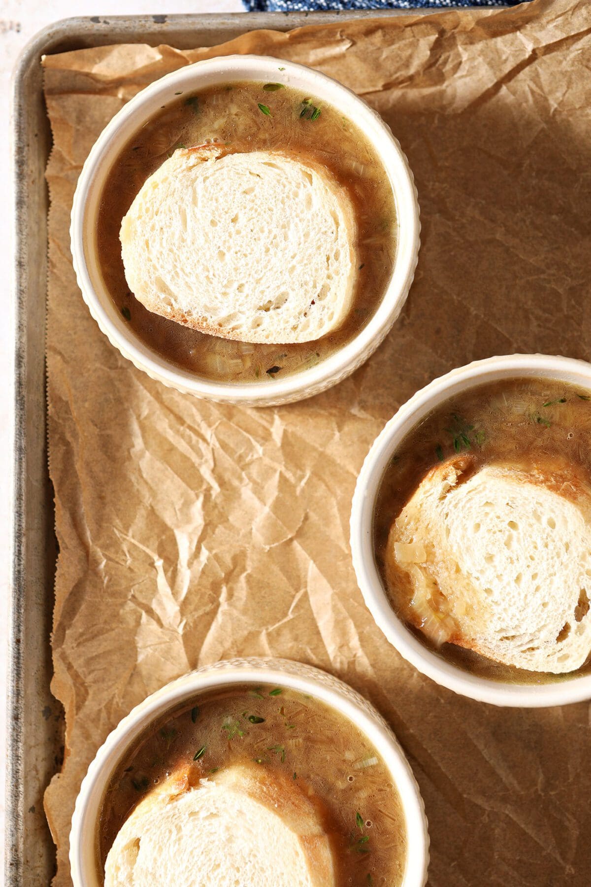 Three containers of French onion soup with slices of bread on top of the soup