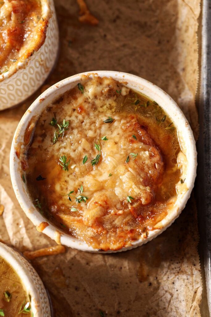 Close up of a bowl of French Onion Soup after broiling with crusty cheese and fresh thyme on top