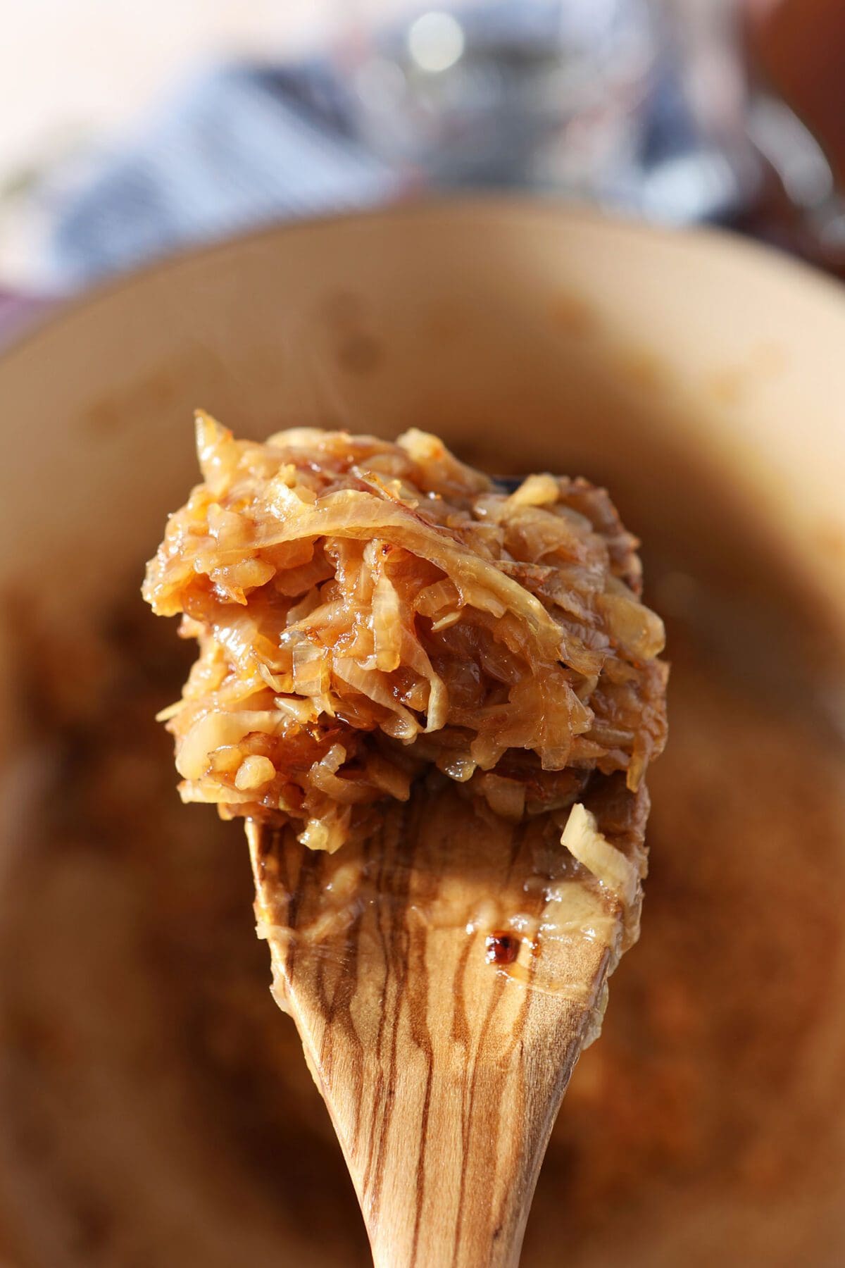 A wooden spoon holds caramelized onions over a Dutch oven