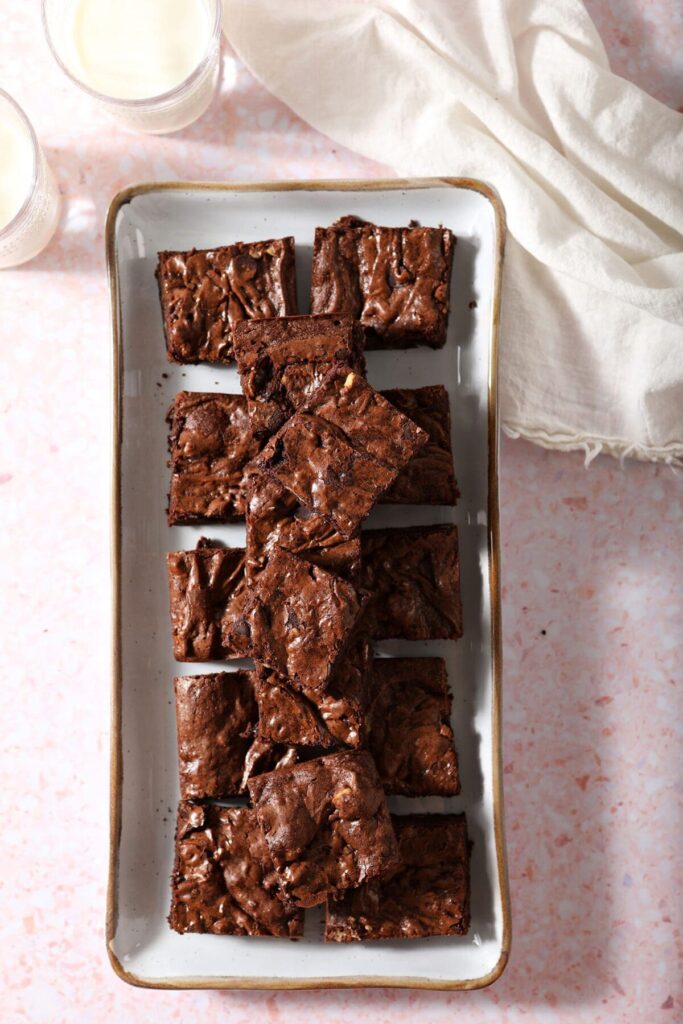 Sliced brownies on a rectangular plate with glasses of milk and a cream-colored linen