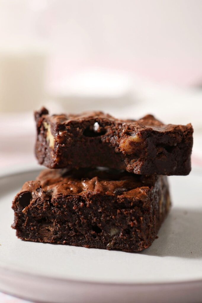 One brownie with a bite taken out of it sits on top of another brownie on a plate