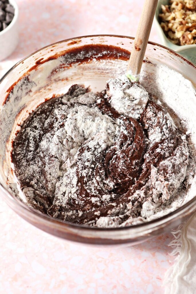 A rubber spatula stirs dry ingredients into the brownie batter