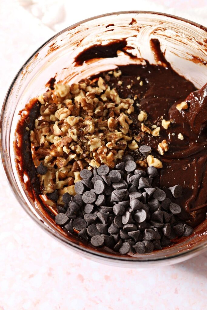 Chopped nuts and chocolate chips sit on top of brownie batter before mixing