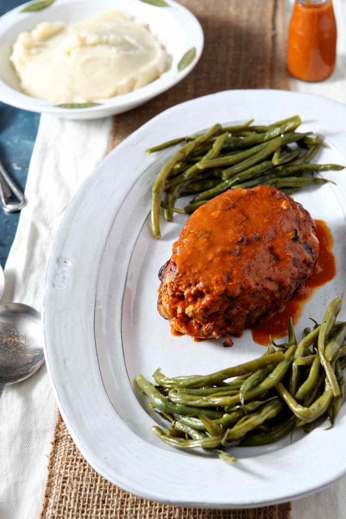 A whole Slow Cooker Turkey Meatloaf sits alongside green beans (with mashed potatoes in the background) before serving.