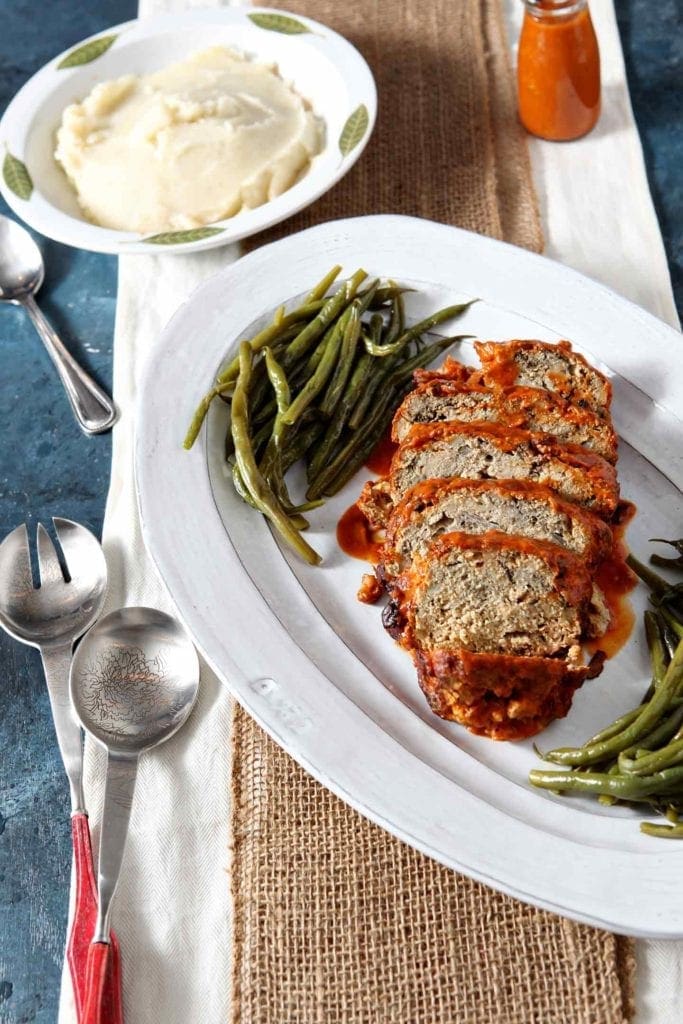 Sliced Slow Cooker Turkey Meatloaf is served on a white platter alongside green beans.