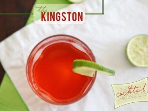 A glass of bright red liquid garnished with a lime round sits on top of a white napkin