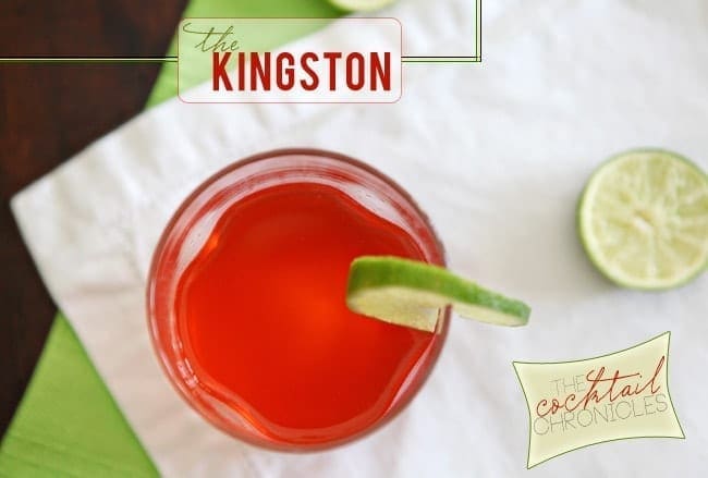 A glass of bright red liquid garnished with a lime round sits on top of a white napkin