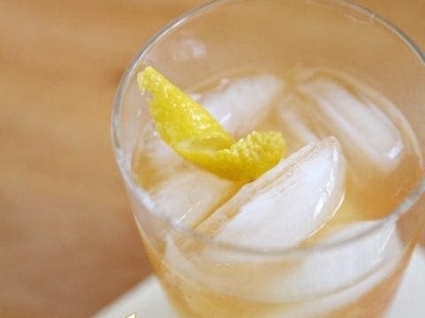 A close up of a cocktail glass holding a golden drink with a lemon twist