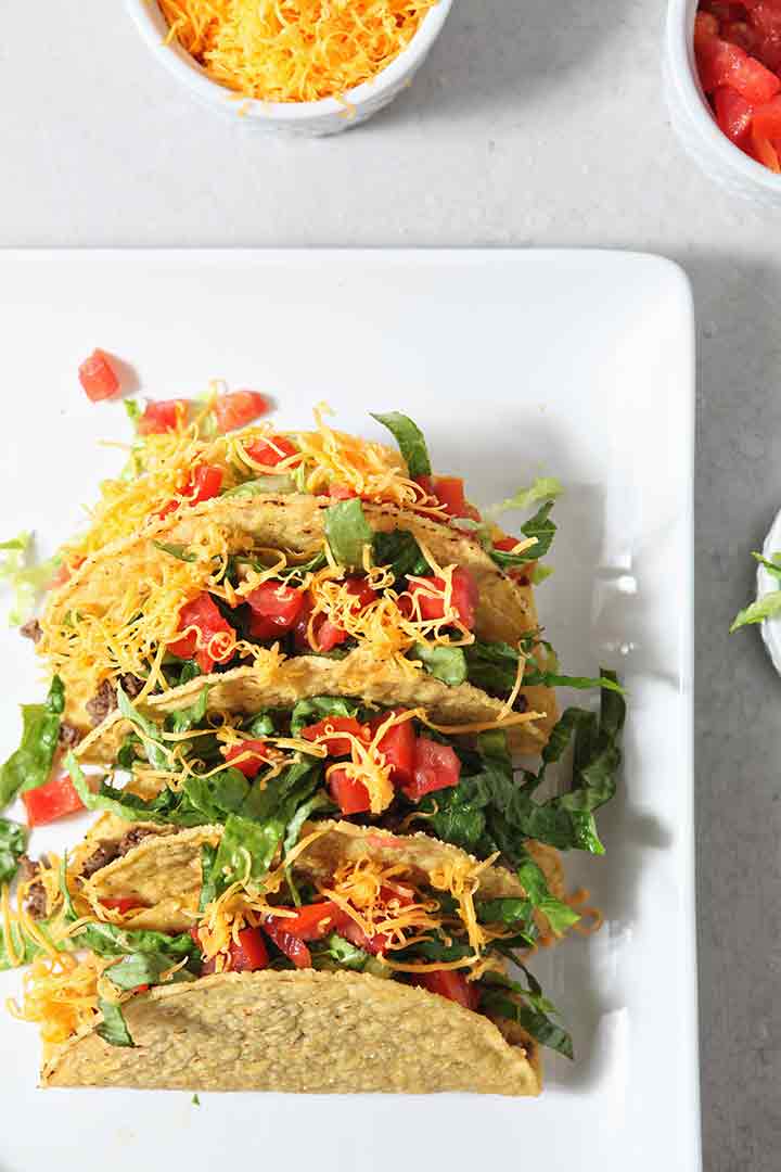 Overhead image of several hard shell Ground Beef Tacos with toppings