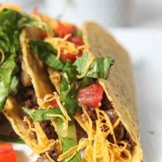 Close up of two hard shell Ground Beef Tacos, topped with lettuce, tomatoes and cheese, on a platter