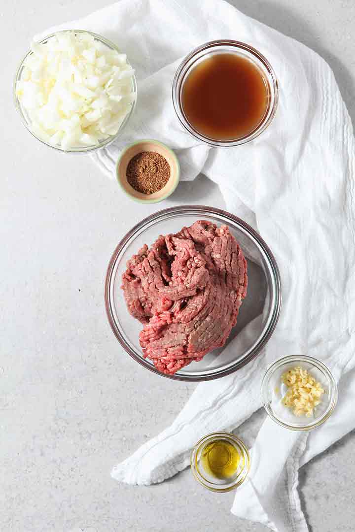 Ground beef and other ingredients are laid out on a surface before cooking