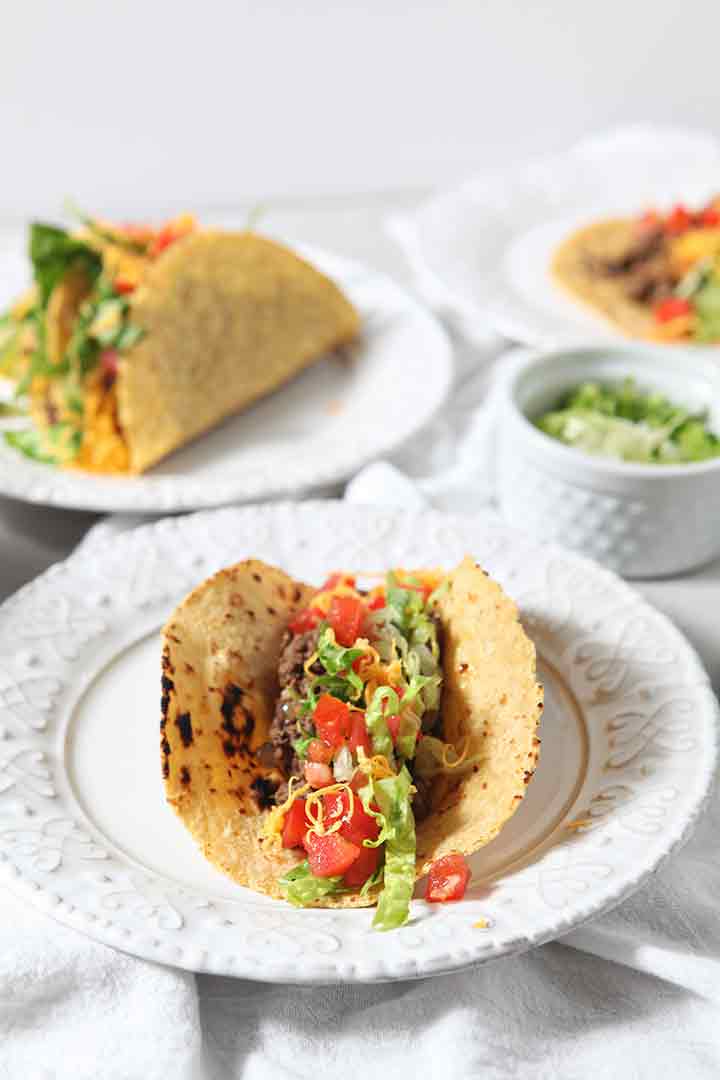 Several Ground Beef Tacos are shown on plates, topped with favorite taco toppings