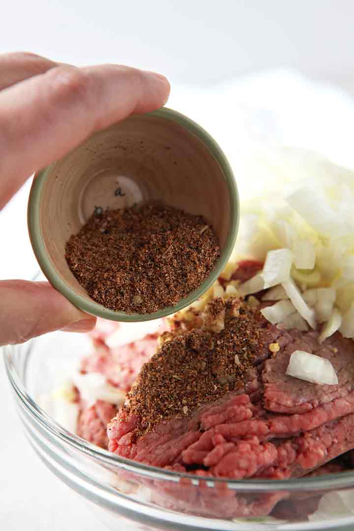 Taco seasoning is sprinkled onto ground beef and onions in a bowl