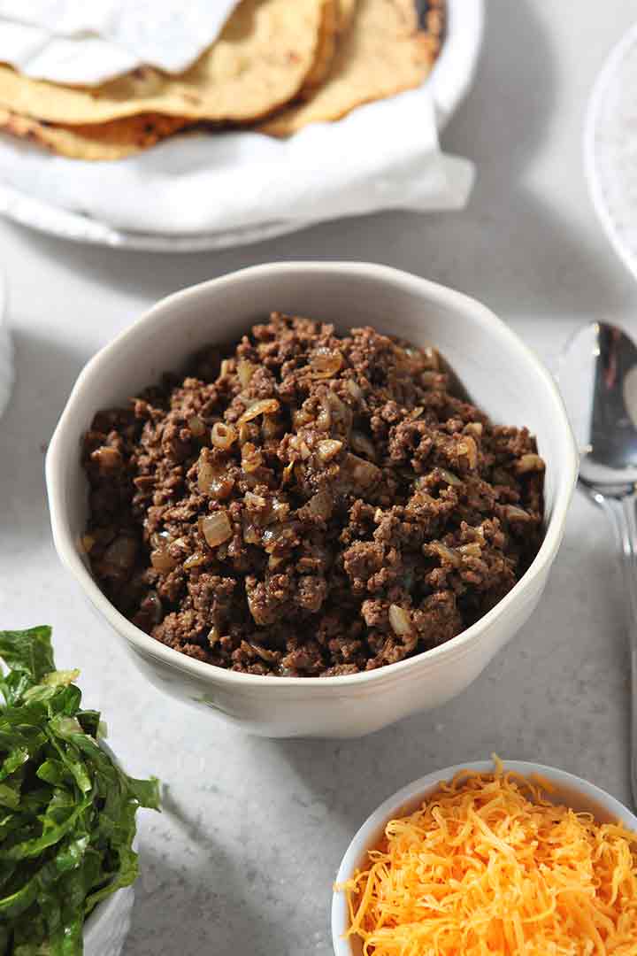 Cooked ground beef and onions are served with taco toppings for guests