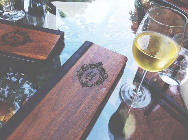 A glass of white wine on a glass table next to a wooden menu