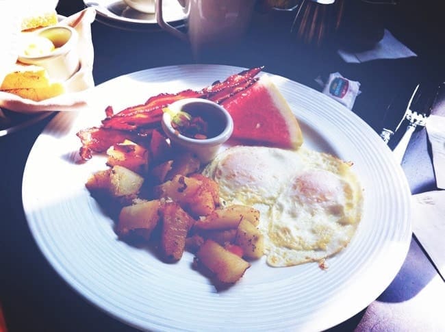 Fried eggs, potatoes, bacon and a slice of watermelon on a white plate