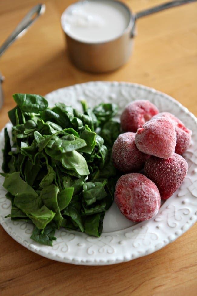 Fresh spinach and frozen strawberries on a white plate