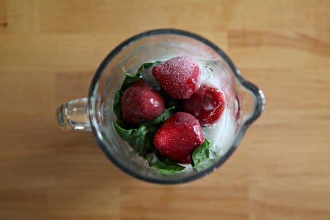 Frozen strawberries, spinach and other ingredients in a blender on a table