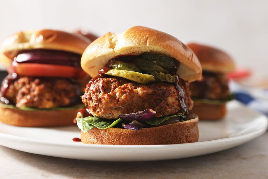 Five BBQ turkey burgers on a white platter with toppings