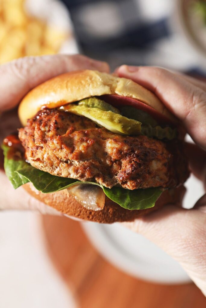 A person holds a BBQ turkey burger in hand above a plate