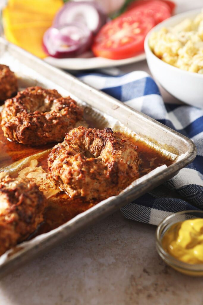 Baked turkey burgers on a sheet pan next to burger toppings