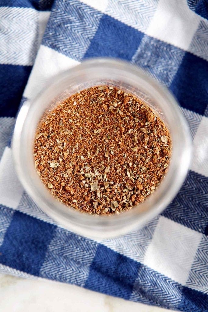 Overhead of a BBQ dry rub blend inside a glass jar on top of a blue and white checked napkin