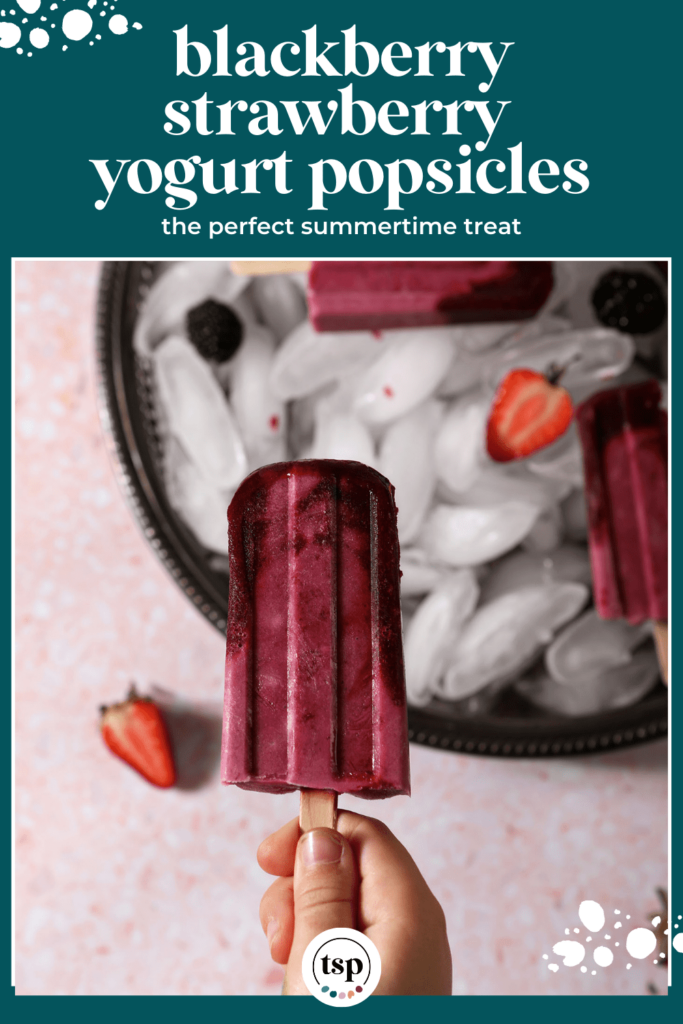 A hand holds a bitten-into ombre berry popsicle in front of a tray of more pops with the text blackberry strawberry yogurt popsicles the perfect summertime treat