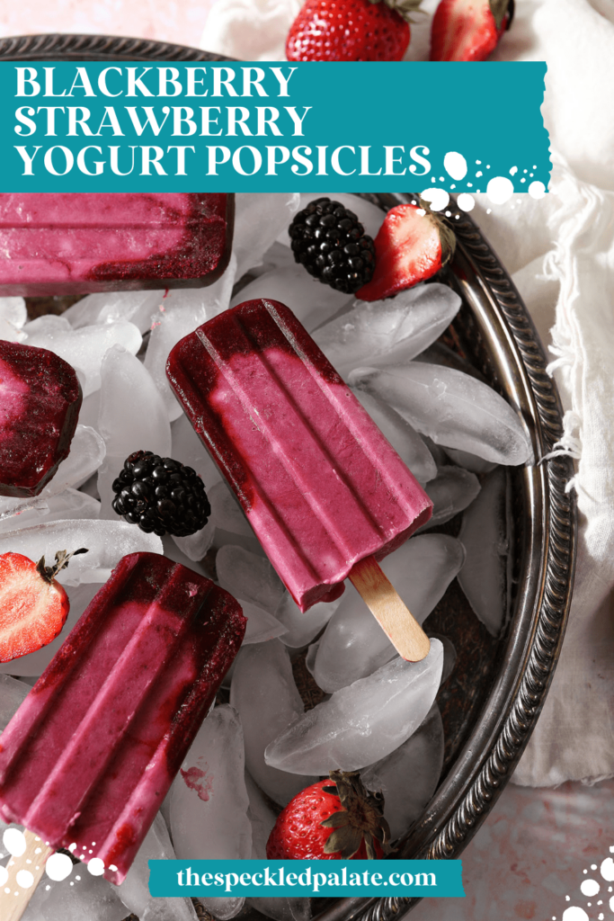 A tray of pink popsicles with berries on top of ice in a silver tray with the text blackberry strawberry yogurt popsicles