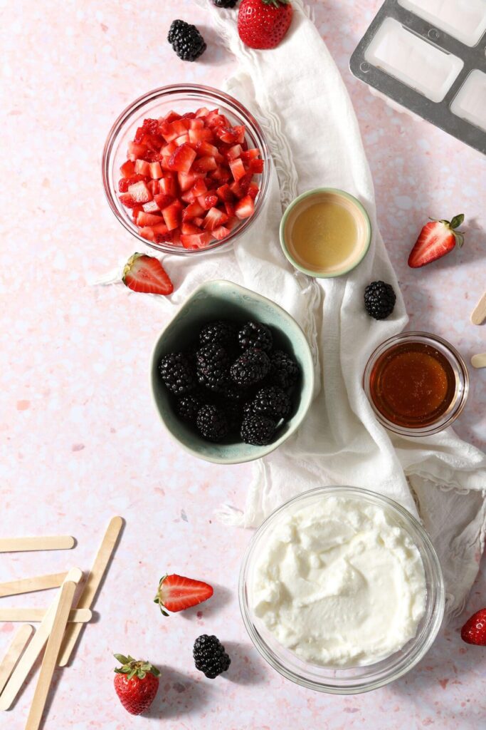 Ingredients to make yogurt ice pops with a cream-colored towel on a pink speckled countertop