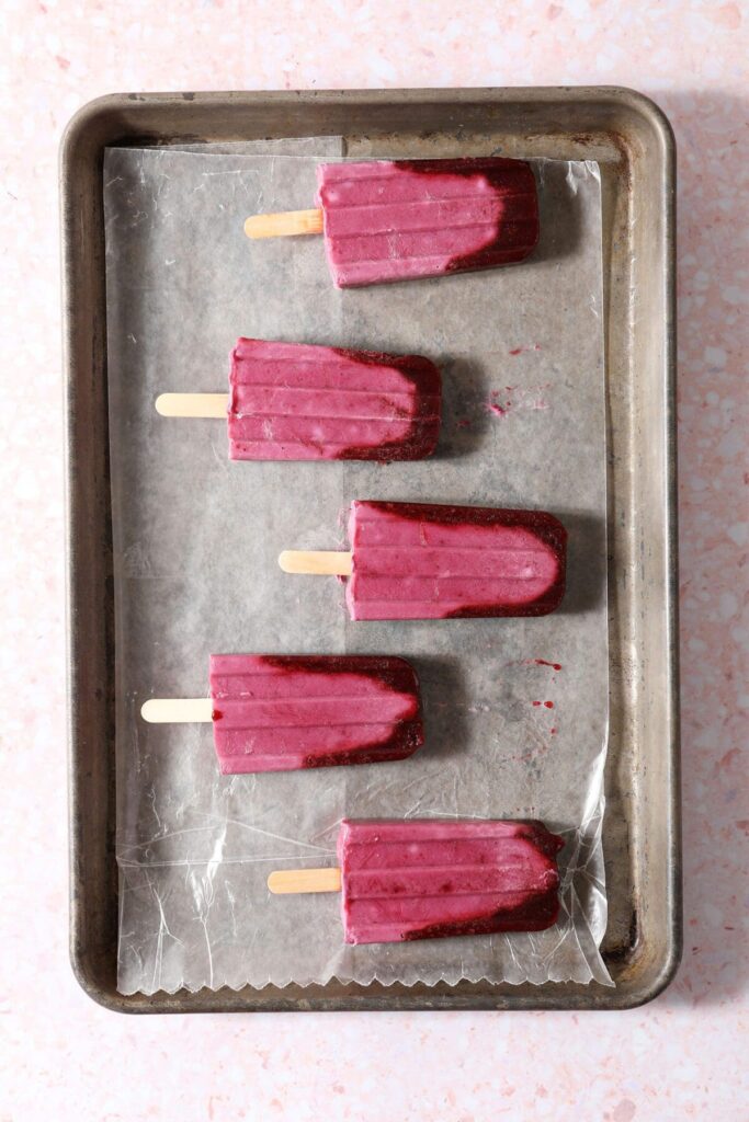 Five ombre pink popsicles on a wax paper-lined sheet pan