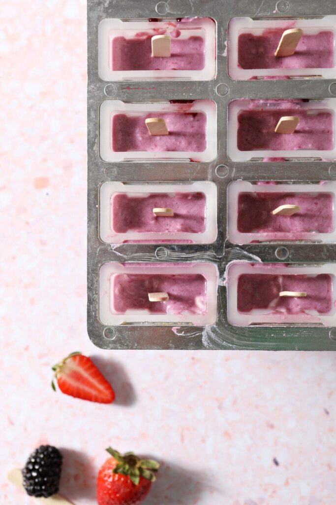 Berry yogurt pops in molds, with wooden sticks from above