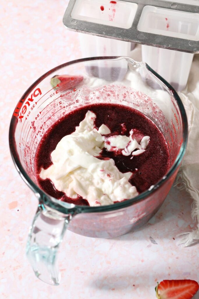 Greek yogurt sits on top of berry puree before mixing