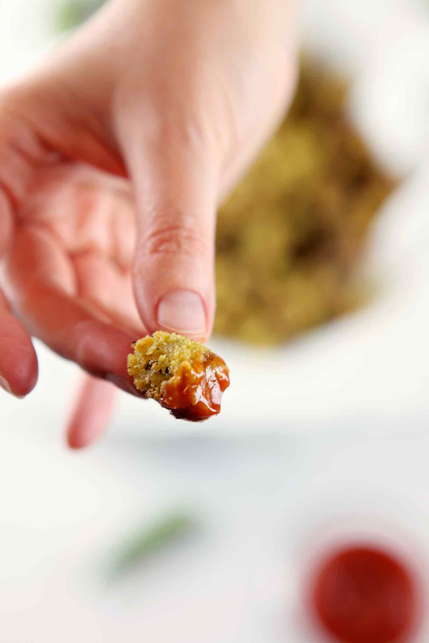 A hand holds a piece of oven fried okra dipped in ketchup