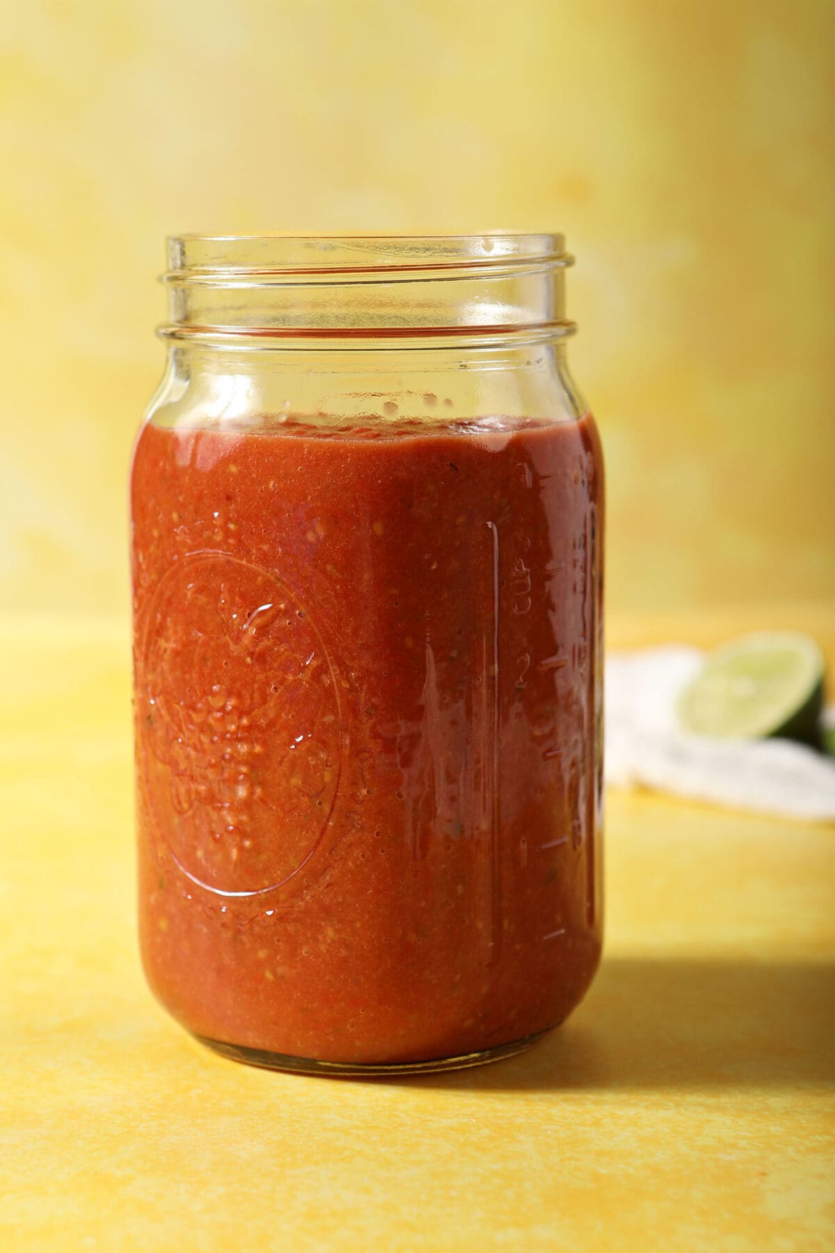 A jar of homemade salsa on a yellow surface