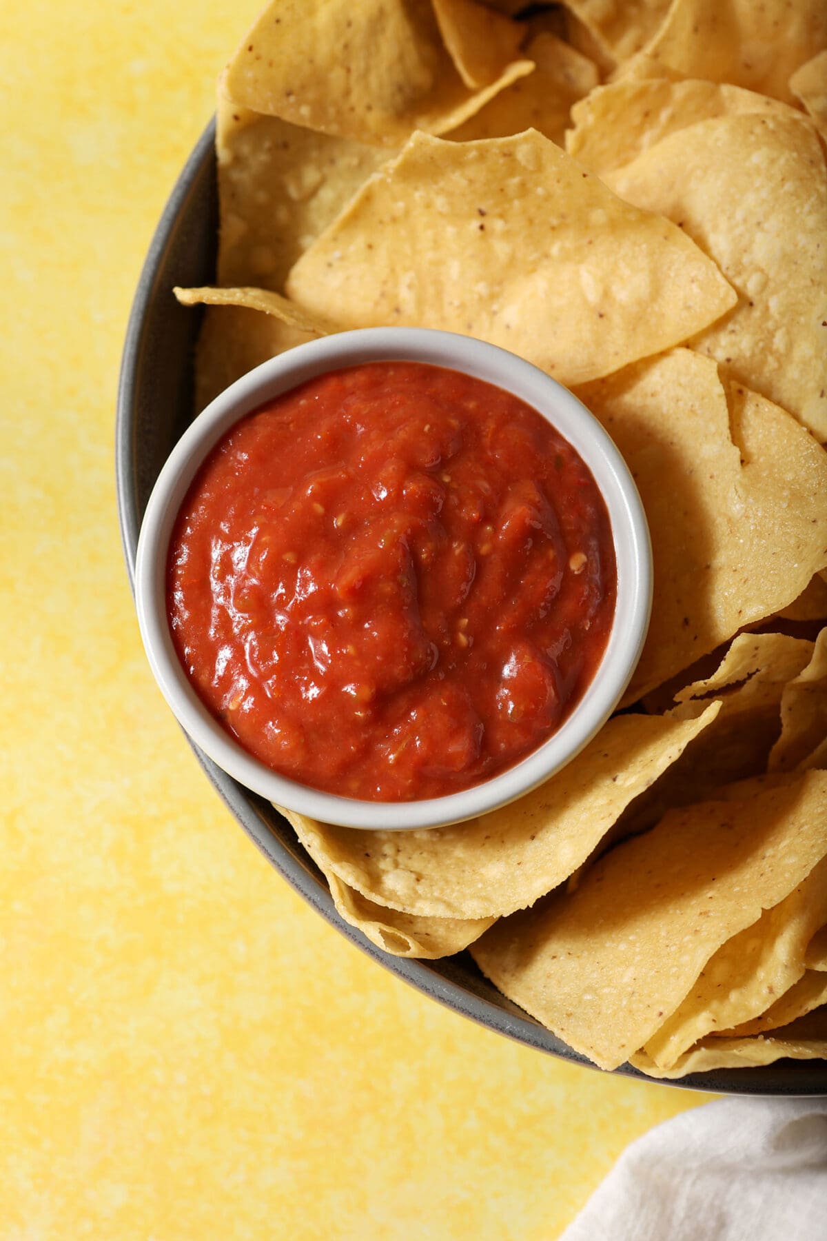 A bowl of salsa surrounded by chips on a yellow surface
