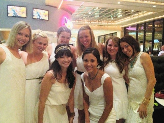 Eight women wear white dresses and smile at the camera