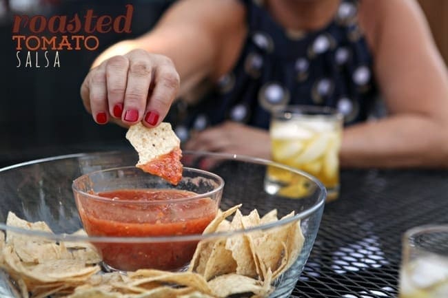 A woman with red nails dips a tortilla chip into a bowl of salsa