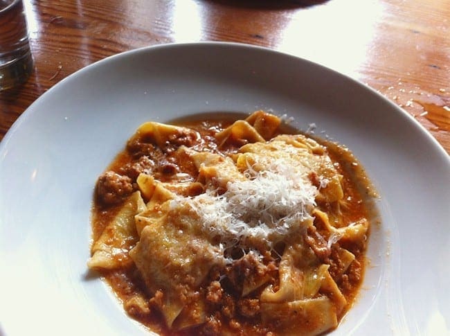 A white bowl holds homemade pasta with a bolognese sauce and a parmesan topping