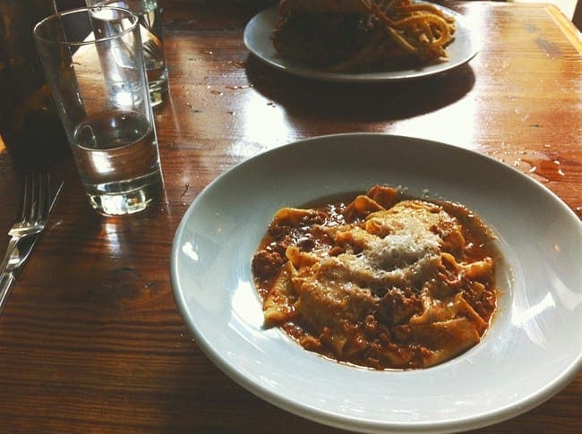 A white bowl holds homemade pasta with a bolognese sauce and a parmesan topping