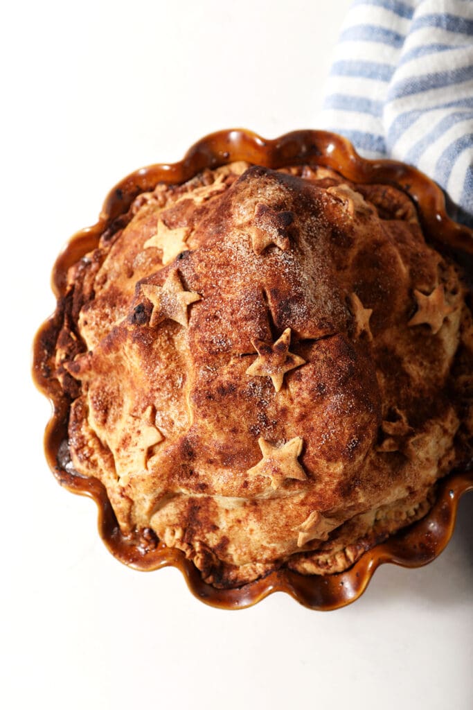 A baked cinnamon apple pie on a white surface with a blue and white striped linen