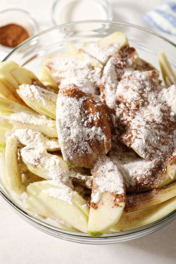 Seasonings on top of apple slices in a bowl before mixing