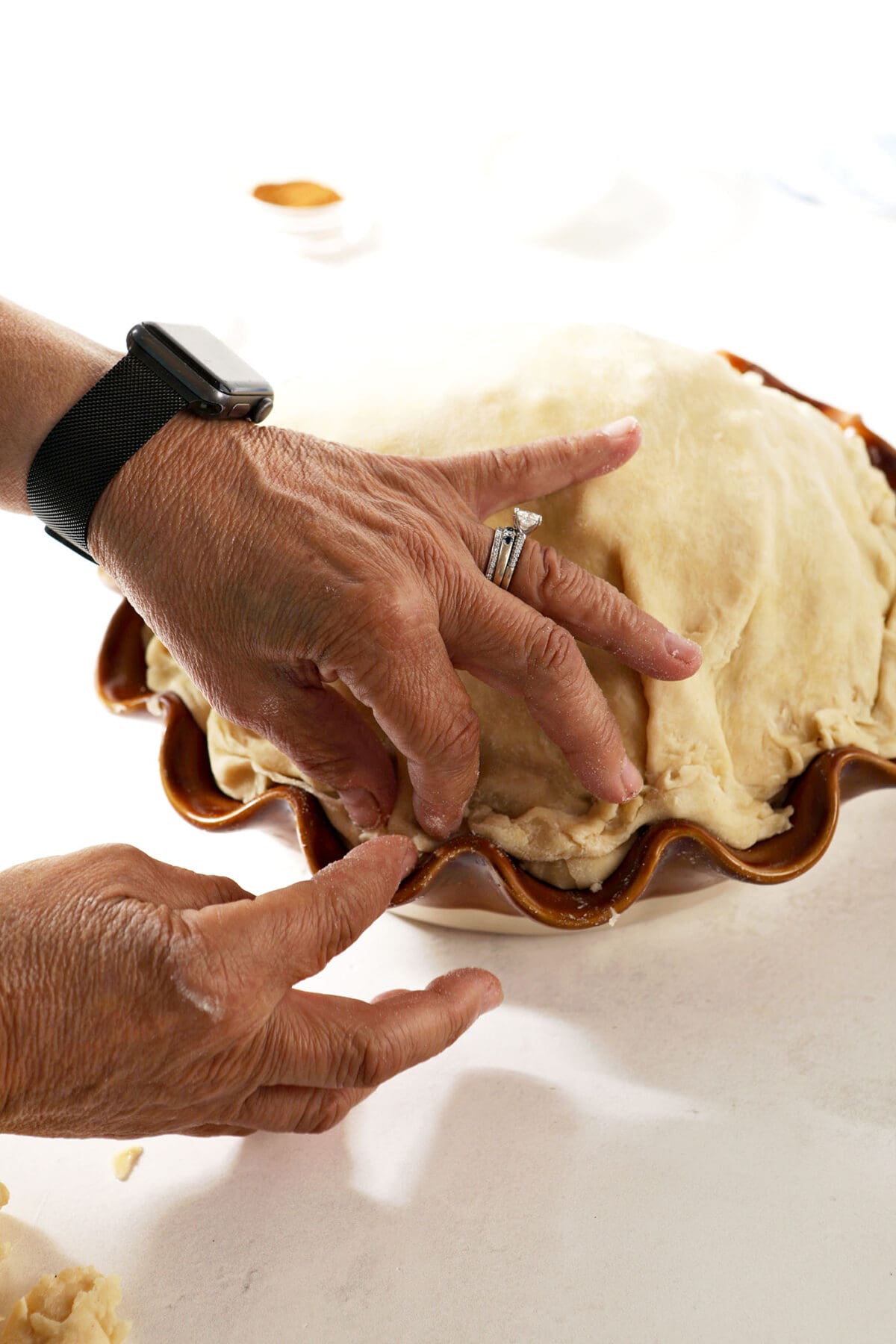 A hand pinches the edges of a pie crust to seal it on a white surface