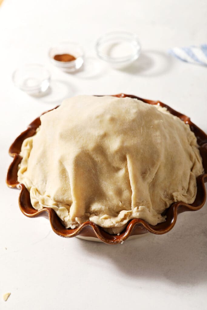 A very tall apple pie on a white surface before baking