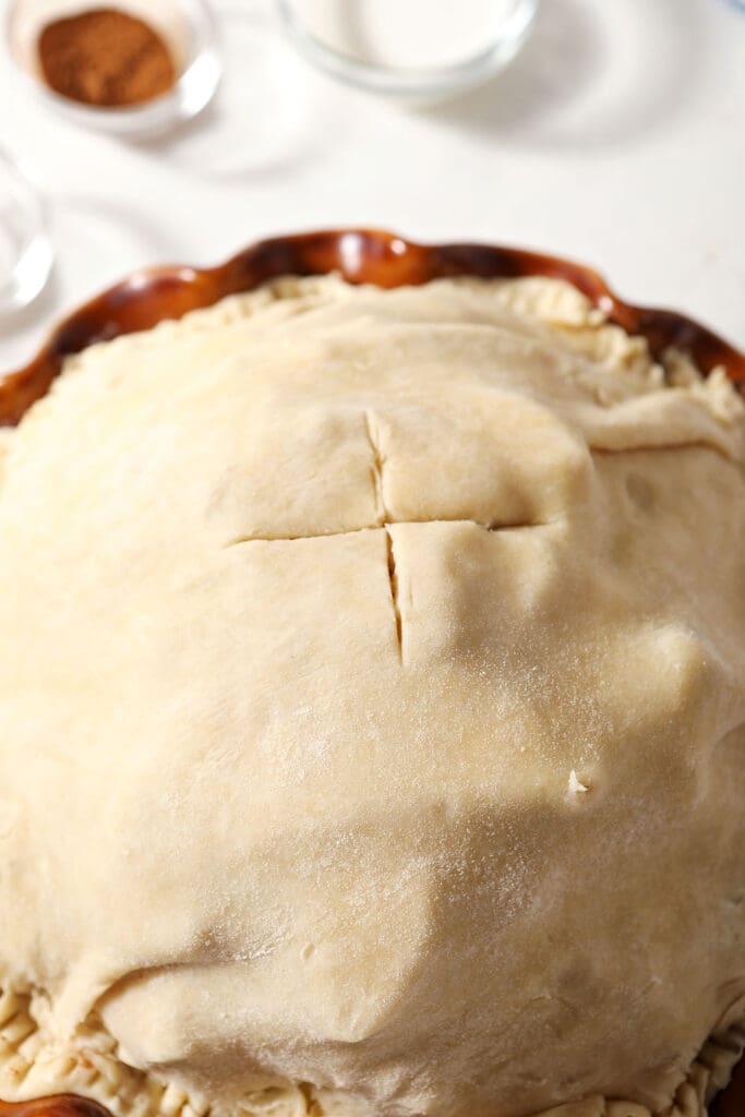An X vent is cut into the top of pie crust on top of an apple pie, before baking