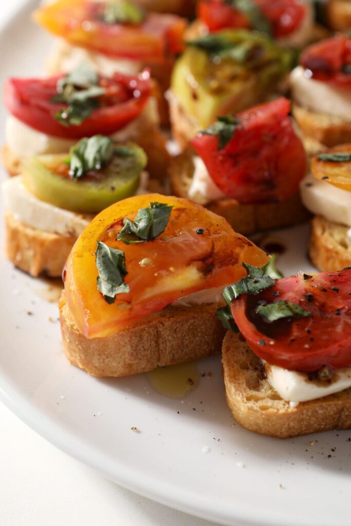 Close up of several Caprese Bruschetta with Heirloom Tomatoes on a white platter