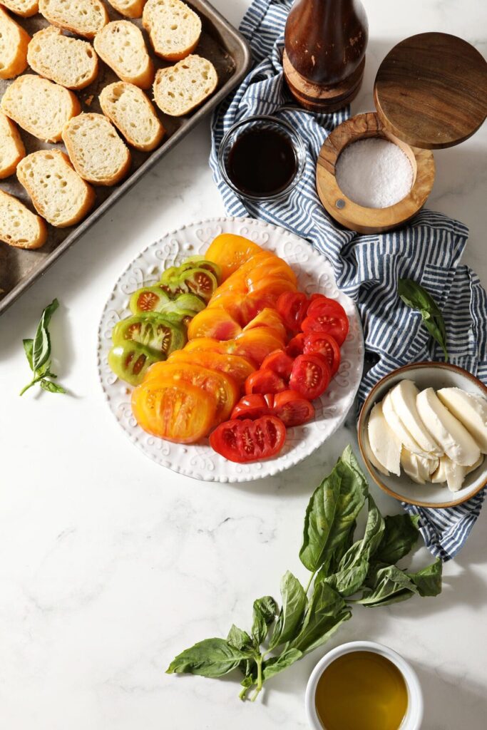 Ingredients to make bruschetta with heirloom tomatoes on plates and bowls on marble