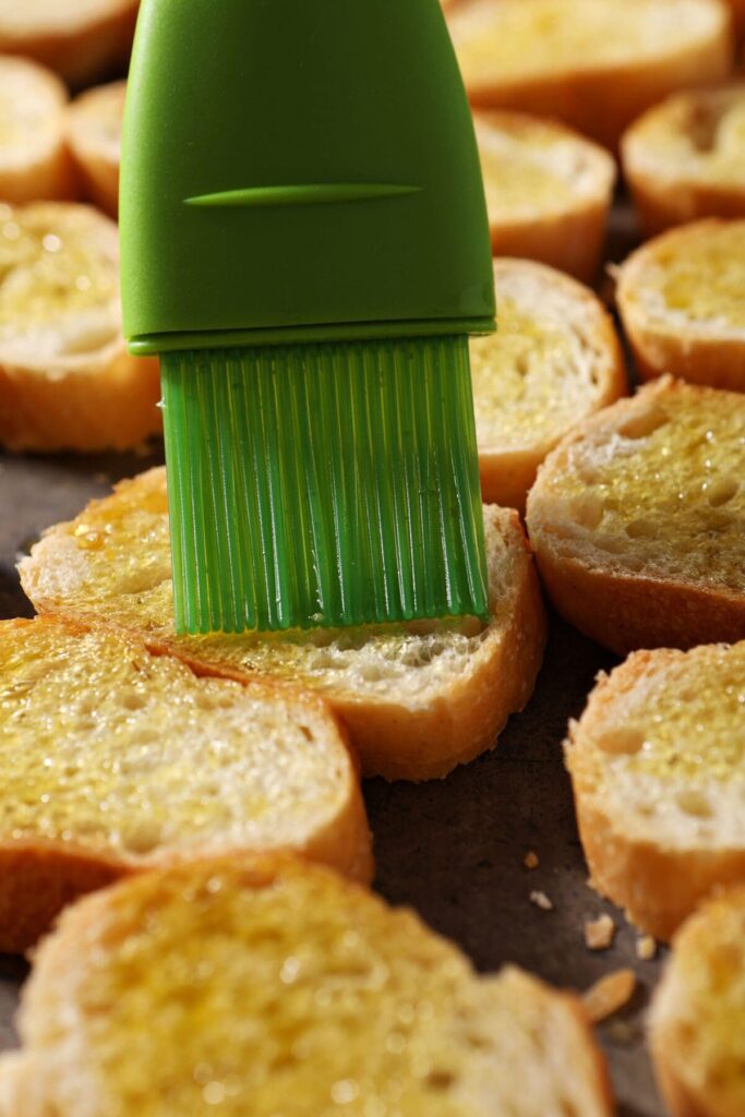 A green silicone brush brushes oil on sliced bread