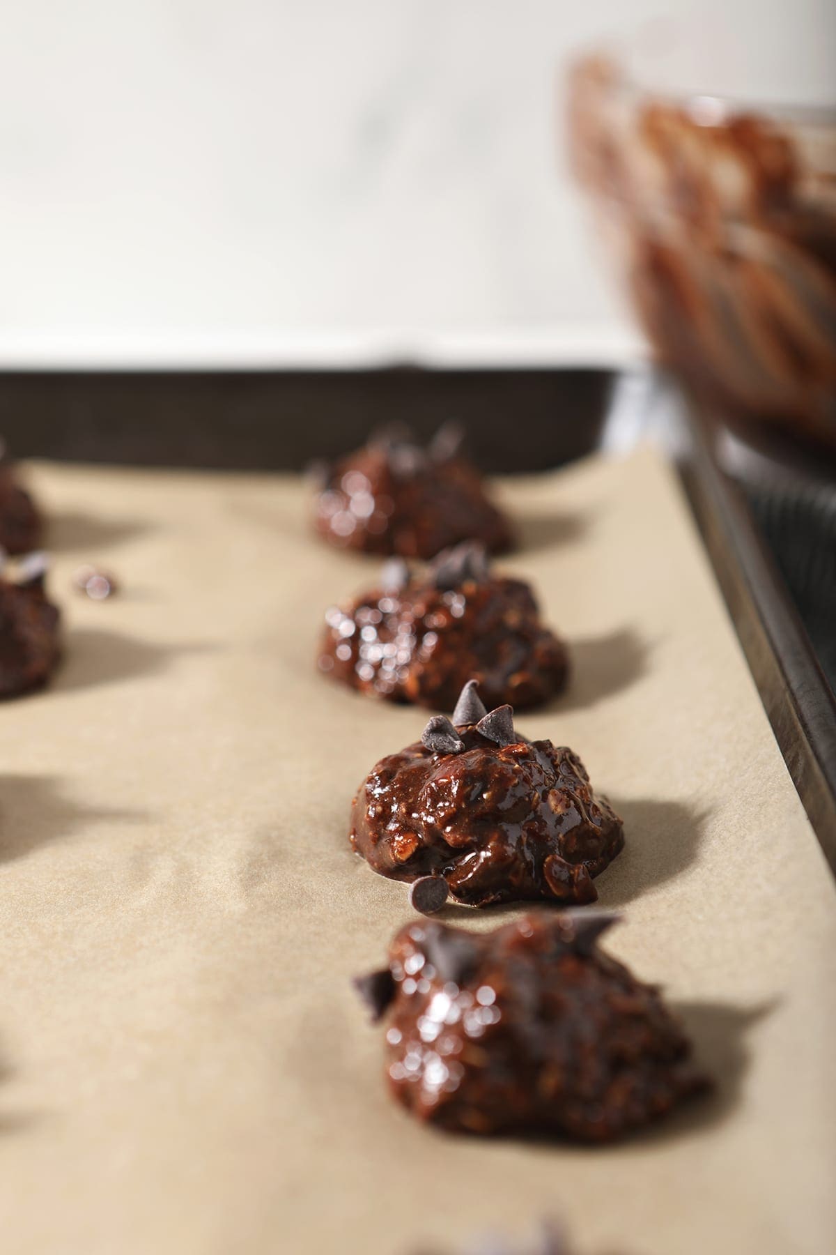 Cookie dough topped with chocolate chips sit on a parchment-lined sheet pan before baking